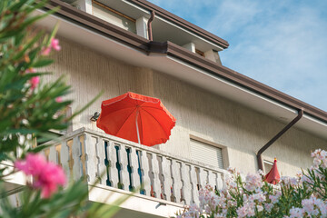 Red umbrella mounted on hotel or house balcony in hot summer day outdoor. Vacation and traveling...