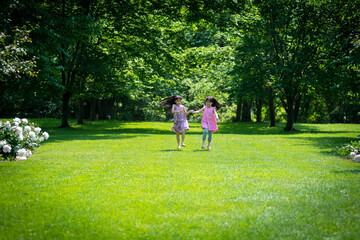 Fototapeta premium Two young asian girls running down middle of garden while holding hands