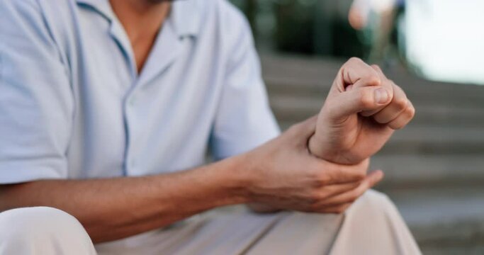 Hand, wrist pain and arthritis with a man outdoor, sitting on steps and feeling his joint for stiffness. Medical, anatomy and osteoporosis with a male suffering from an injury or broken bone