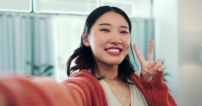 Face, woman and peace for selfie in home, smile and fun with live streaming vlog in living room. Portrait, profile picture and happy asian female show v sign, hand emoji and happiness on social media