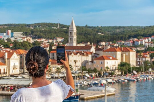Back shot of a girl taking photos by phone of the idyllic coastal town of Supetar on Brac in Croatia