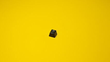Black ''escape'' keyboard key isolated on yellow background Top view. Copy space.
