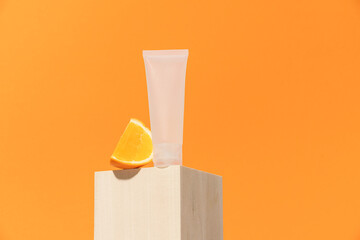 White tube and orange slice on wooden podium and orange background. Vitamin C beauty product concept