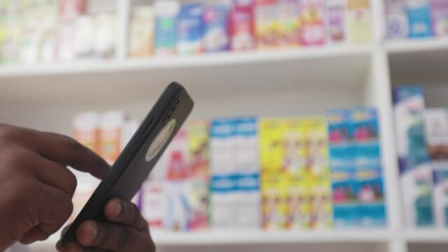 
Close Up, Hands of  Professional Black African Pharmacist Using Smartphone to check availability of  Medicine, Drugs, Healthcare Products in Drugstore Store 