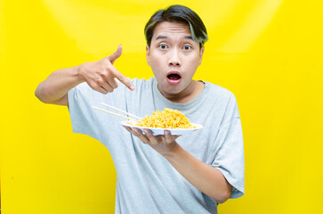 Happy euphoric asian young man in grey tshirt eating instant fried noodle using bamboo chopstick...