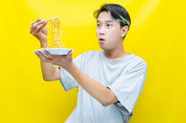 Happy euphoric asian young man in grey tshirt eating instant fried noodle using bamboo chopstick...