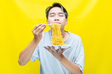 Happy euphoric asian young man in grey tshirt eating instant fried noodle using bamboo chopstick...