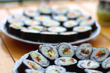Plates with homemade sushi rolls on wooden table. Tuna and vegetable sushi, and vegetarian cream cheese and vegetable sushi. Selective focus.