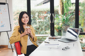 Asian woman is smelling the coffee. Young businesswoman drinking coffee in her office. Woman enjoy...
