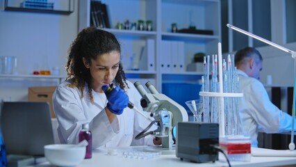Chemical lab worker adding a drop of cosmetic sample at test glass, examining under microscope