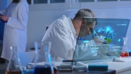 Lab worker looking at sample in microscope, unknown matter analysis on holographic screen