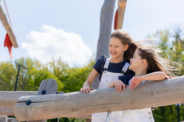 two happy girls are playing on the playground in the summer, looking into the distance on a wooden children's ship. International Children's Day. Earth Day