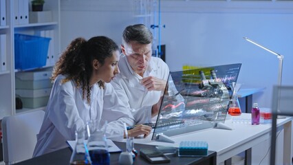 Two lab scientists looking at results of experiment on computer screen, advanced technology