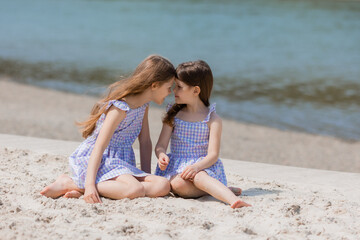 happy little girls with long hair play on a sandy beach near the sea on a sunny day. Children's Day.Space for text