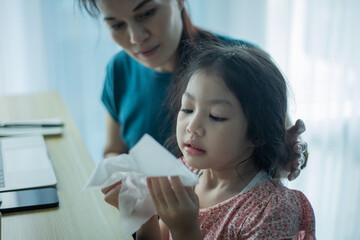 Mother helping her daughter blow her nose.