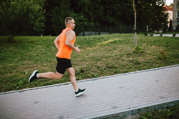 Young guy is exercising outdoors. Male runner jogging in the park. Healthy lifestyle concept....