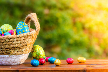 Easter eggs in basket on wooden table banner. Easter season banner with green nature bokeh background. Colorful decorated eggs in wicker basket. Spring season decoration for web banner