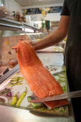 a seller in a fish store holds a large piece of salmon fillet in his hand