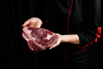 The chef is holding a ribeye beef steak. Aged and matured steak. Meat. On a black background.