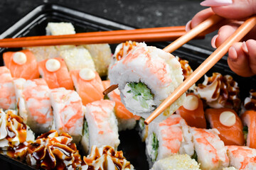 A sushi roll with seafood is held with chopsticks. On a black stone background.