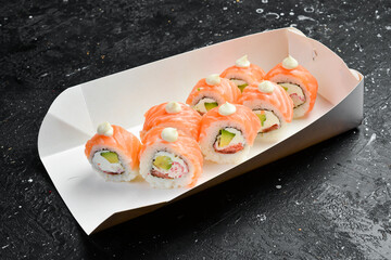 Sushi rolls with cheese and crab and caviar, Japanese food. Delivery. Disposable tableware. On a black stone background.