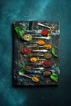 Set of spices and herbs in vintage spoons. Colorful various spices for cooking. On a black slate background.