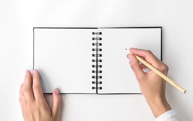 woman writing notes on clean white paper on square spiral notepad, top view