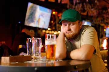 Drunk male customer sleeps on the bar counter with a beer at the pub. Alcohol addiction, drinking problem