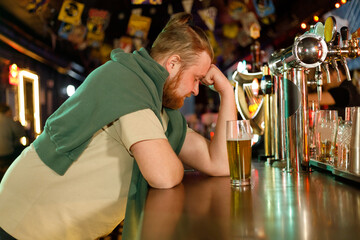 Alcoholism concept. Young man drinking alcohol too much. Stressed drunk man sitting alone with beer in bar