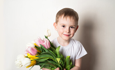 Portrait of a smiling boy with freckles in a white t-shirt with a bouquet of tulips on a white background. The concept of spring, holiday, joy, life.