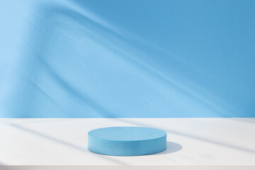 Round cylinder podium for products or cosmetics against light blue background with leaves shadows.	

