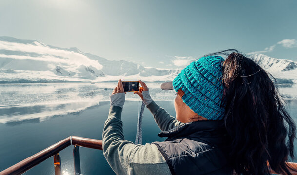 Female Tourist On Luxury Antarctica Cruise Ship Looking Out At The Stunning Scenic Arctic Landscape, As She Takes a Photo with her Phone, Landscape Shot