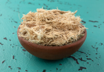 Small bowl filled with shredded slippery elm bark on a tabletop side view.