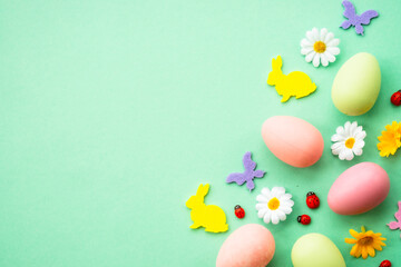 Easter background. Eggs, rabbit, spring flowers and butterfly. Flat lay mock up at green background.
