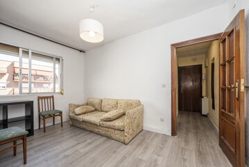 Living room furnished with a solitary sofa in printed fabric of dubious taste, sapele wood doors and gray wooden floors