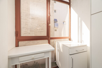 Corner of a kitchen with white furniture next to a window with red aluminum and glass