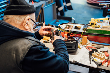 Retired elderly man making ship model building handcraft on the table in his garage. Pensioner...