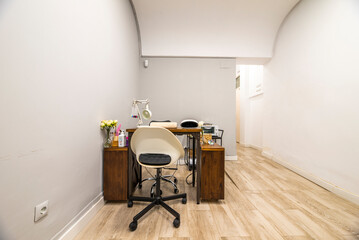 Wooden table of a beauty salon dedicated to nail treatment with swivel chair with black leg and white synthetic seat