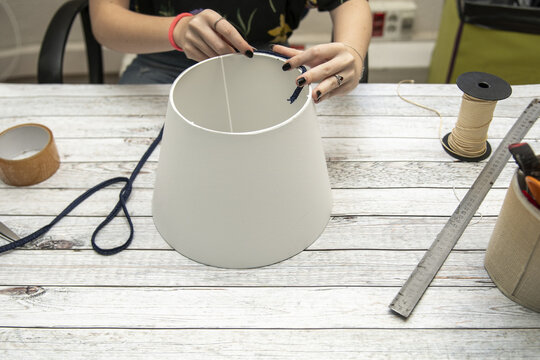 Hands of a woman making a lampshade on a white table