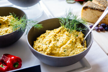 gelber Hummus in einer dunklen Keramikschüssel mit Dill garniert