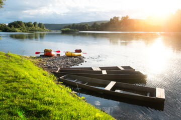 Orange and yellow packrafts rubber boats on a sunrise river near old wooden boats. Packrafting and active lifestile concept