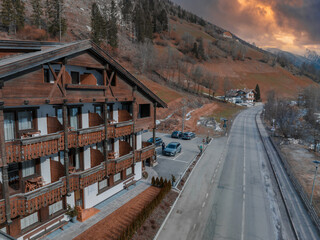 Fototapeta premium Typical wooden alpine house decorated with flowers in the middle of the village on a cloudy winter day, Tyrol, Italy. Aerial view.
