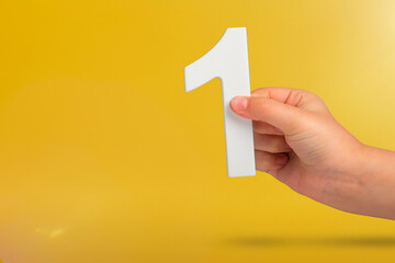Number one in hand. A hand holds a white number one on a yellow background with copy space. Concept...