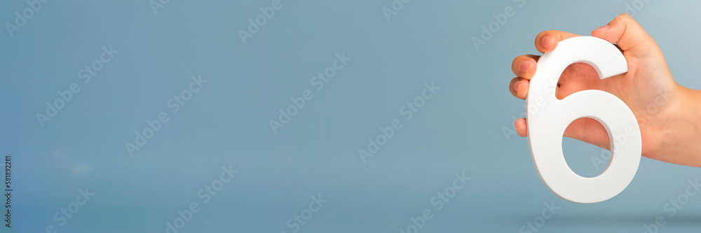 Aufkleber Number six in hand. A hand holds a white number 6 on a blue background with copy space. Concept with number six. 6 percent, birthday 6, sixth grade, in sixth grade