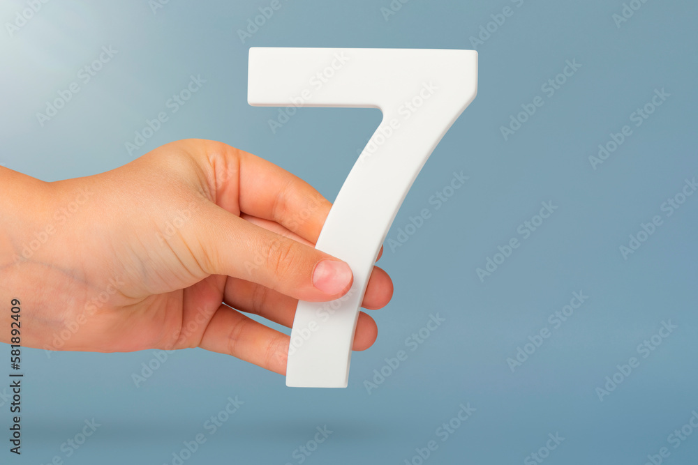 Aufkleber Number seven in hand. Hand holding white number 7 on blue background with copy space. Concept with number seven. Birthday 7 years, percent, seventh grade or day.