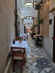 Fototapeta na wymiar Charming white tiny street with a restaurant at the coastal Italian town of Monopoli, Puglia, Italy, Italia