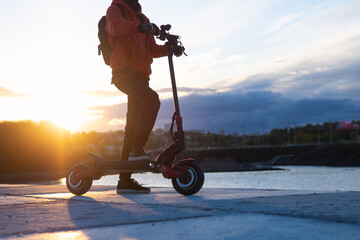 A man on a powerful modern electric scooter on the road against the backdrop of the city at sunset