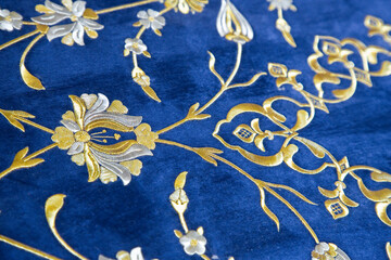 Old Turkish embroidered fabric with golden geometric and floral decorations against a blue...