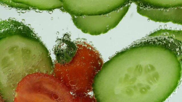 Slices of fresh cucumbers and tomatoes in clear water