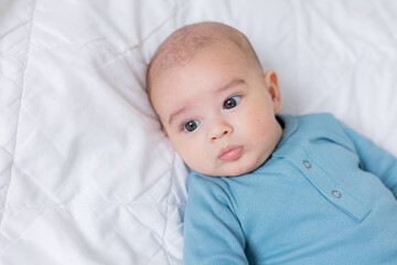 cute baby in a blue bodysuit is lying in bed. Top view